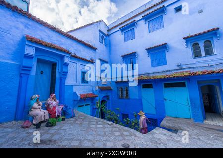 Chefchaouen, Marokko - 25. März 2024: Einheimische Frauen ruhen sich an einem Eingang inmitten blau gestrichener Gebäude aus. Die einzigartige blau-weiße Architektur der Stadt c Stockfoto