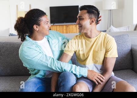 Ein vielseitiges schwules Paar genießt während eines Videoanrufs einen gemütlichen Moment zu Hause. Sie teilen eine warme, liebevolle Verbindung auf dem Sofa und strahlen Glück aus. Stockfoto