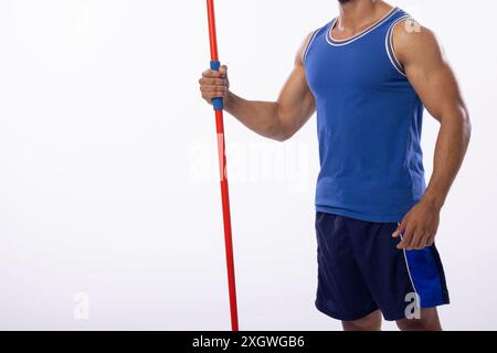 Junger birassischer Mann, der einen Speer auf weißem Hintergrund hält, mit Kopierraum. Sportliche Kleidung deutet auf ein Sporttraining oder einen Fitnesskontext in einem Indoo hin Stockfoto