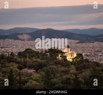 Blick auf das nationale Observatorium von Athen auf dem Nymphen-Hügel mit Lichtern vor Sonnenaufgang, mit Stadt Athen und Bergen im Hintergrund und Bäumen im Hintergrund Stockfoto