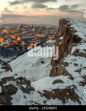 Vertikaler Blick auf Edinburgh, Schottland, mit Schnee bedeckt und mit Stadtlichtern an, von den Salisbury Crags im Holyrood Park an einem Wintermorgen Stockfoto