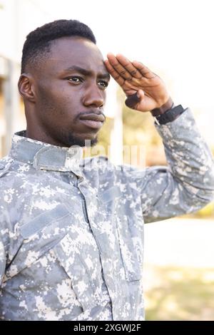 Fokussierter afroamerikanischer Soldat in Uniform, der draußen grüßt. Militärdienst, Armee, Arbeit, Aufmerksamkeit und Pflicht, unverändert. Stockfoto