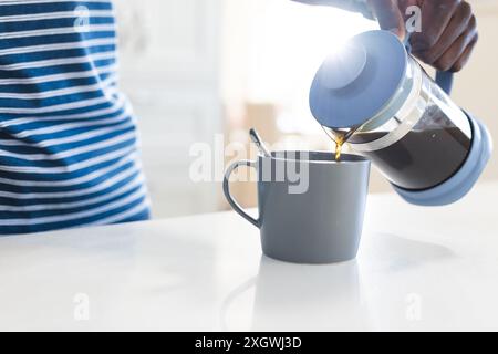 Mitte des afroamerikanischen Mannes, der Kaffee aus dem Café in der Küche gießt. Erfrischung, Morgen, Hausleben und Lebensstil, unverändert. Stockfoto