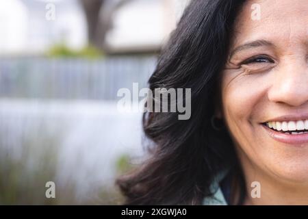 Halbporträt einer glücklichen älteren birassischen Frau mit langen schwarzen Haaren, die draußen lächelt, Kopierraum. Wohlbefinden, Gesundheit und aktiver Lebensstil der Senioren Stockfoto