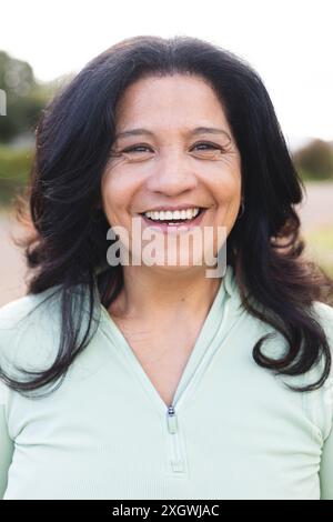 Porträt einer glücklichen älteren Frau mit langen schwarzen Haaren, die draußen lächelt. Wohlbefinden, Gesundheit und aktiver Lebensstil der Senioren, unverändert. Stockfoto