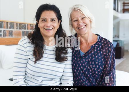 Porträt von zwei glücklichen, verschiedenen älteren Freundinnen, die sich im Wohnzimmer umarmen und lächeln. Freundschaft, häusliches Leben und Seniorenleben, unverändert. Stockfoto