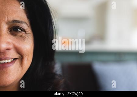 Halbporträt einer glücklichen älteren birassischen Frau mit schwarzen Haaren, die zu Hause lächelt, Kopierraum. Wohlbefinden, häusliches Leben und Lebensstil der Senioren, unverändert. Stockfoto