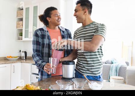 Schwule Biracial und nahöstliche Paare machen Smoothies in einer Küche. Sie teilen einen freudigen Moment, während sie zusammen ein gesundes Getränk zubereiten. Stockfoto