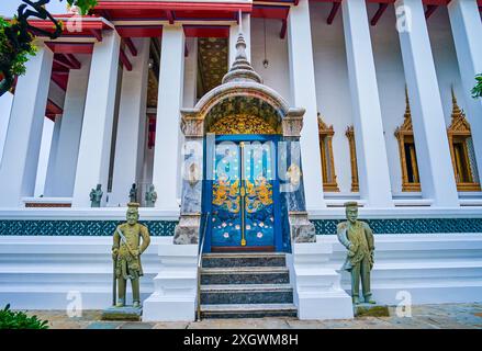 Die farbenfrohe Seitentür zu Ubosot von Wat Suthat mit zwei Wächtern, Bangkok, Thailand Stockfoto