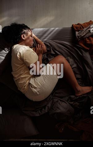 Draufsicht einer jungen depressiven Frau mit geknickten Beinen und geschlossenen Augen auf dem Bett liegend und an posttraumatischem Syndrom leidend Stockfoto