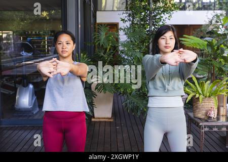 Porträt fokussierter asiatischer Freundinnen, die Yoga üben und sich im Garten zu Hause dehnen. Fitness, Bewegung, häusliches Leben, Freundschaft, Aktivität und Stockfoto