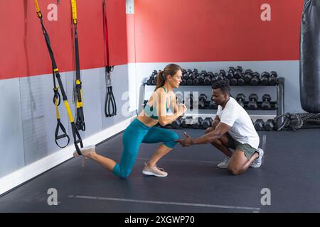 Eine fitte junge kaukasische Frau trainiert mit einem fitten Afroamerikaner im Fitnessstudio. Sie konzentrieren sich auf Fitness, wobei ein persönlicher Trainer die Übung leitet. Stockfoto
