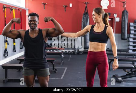 Ein passender Afroamerikaner und eine junge Kaukasierin im Fitnessstudio. Mit einer freundlichen Geste zeigen sie den Fitnessfortschritt. Stockfoto