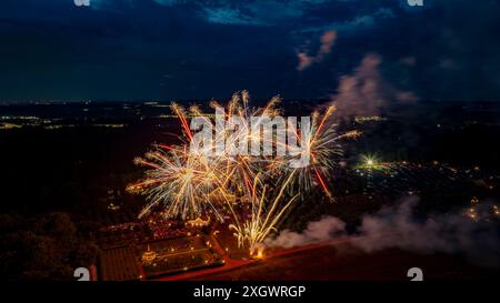 Farbenfrohe Feuerwerke erleuchten den Nachthimmel über Einem gut beleuchteten Anwesen, umgeben von Bäumen, Feldern und fernen Stadtlichtern und schaffen Eine große und festliche Festszene. Stockfoto