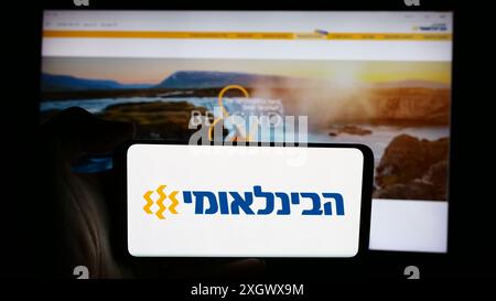 Person, die ein Mobiltelefon mit dem Logo der First International Bank of Israel Ltd. (FIBI) vor der Webseite hält. Schwerpunkt auf dem Display des Telefons. Stockfoto