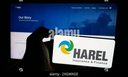 Person, die ein Mobiltelefon mit dem Logo von Harel Insurance Investments and Financial Services Ltd. Vor der Webseite hält. Schwerpunkt auf dem Display des Telefons. Stockfoto