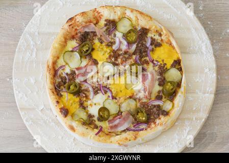 Blick von oben auf eine frisch gebackene Pizza mit verschiedenen Belägen, darunter Pilze, Speck und Käse, serviert auf Pergamentpapier auf einer Marmoroberfläche. Stockfoto