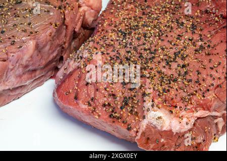 Zwei rohe Steaks mit Gewürzen bereit zum Barbeque auf weißem Hintergrund aus nächster Nähe. Zwei rohe Steaks auf einem weißen Schneidebrett mit Steakgewürzen. Stockfoto