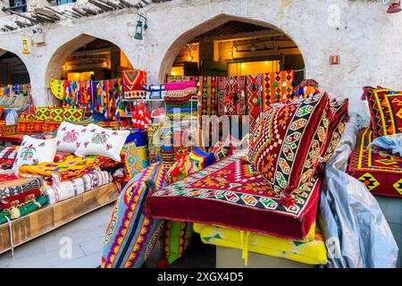 Eine farbenfrohe Ladenfront im Freien, in der farbenfrohe Stoffe auf Decken, Teppichen und Kissen auf dem Souq Waqif Marktplatz von Doha Qatar verkauft werden. Stockfoto