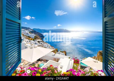 Blick von einem offenen Fenster mit blauen Fensterläden und Blumen auf die Ägäis, die Caldera und die weiß getünchte Stadt Oia, Santorini, Griechenland. Stockfoto