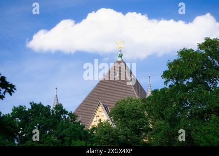 Eine Wolke über dem Dach mit dem davidstern der kölner Synagoge hinter den Bäumen des rathenauplatzes Stockfoto