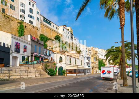 Die weiß getünchten Gebäude an den Klippen mit Straßencafés und Geschäften unten am Hafen von Mahon, auf der Baleareninsel Menorca Spanien. Stockfoto