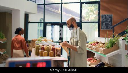 Mann füllt Papiertüte mit Pasta, um die richtige Menge für gesunde Mahlzeit zu kaufen, gießt natürliche Waren verkauft als Massenprodukte in wiederverwendbaren Gläsern. Kunde geht einkaufen. Stockfoto