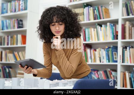 Architektin, die ein Tablet am Bibliothekstisch benutzt, während sie ein Stadttraining erstellt Stockfoto
