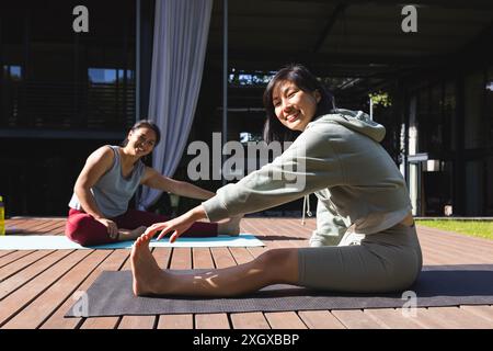 Porträt glücklicher asiatischer Freundinnen, die zu Hause Yoga üben und sich im Garten dehnen. Fitness, Bewegung, häusliches Leben, Freundschaft, Aktivität und li Stockfoto