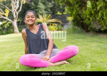 Teenager-Biracial-Mädchen genießt einen sonnigen Tag im Freien mit viel Kopierraum, unverändert. Sie sitzt auf dem Gras, strahlt Positivität und Entspannung aus Stockfoto