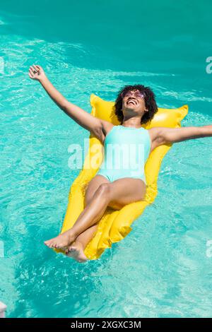 Die junge Frau genießt einen sonnigen Tag, der in einem Pool schwimmt. Ihre entspannte Pose auf dem aufblasbaren Gerät lässt eine entspannte und unbeschwerte Sommerstimmung vermuten. Stockfoto