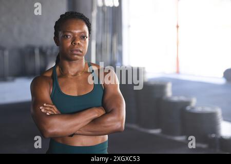 Eine fitte afroamerikanische Frau steht im Fitnessstudio mit blauem Hintergrund. Ihre starke Körperhaltung und ihr straffer Körper unterstreichen ihr Engagement für Fitness, unveränderlich Stockfoto