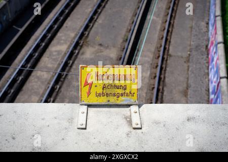 Gelbes Schild mit roter Aufschrift in deutscher Hochspannung Achtung Lebensgefahr auf einer Brücke über eine Eisenbahnstrecke Stockfoto