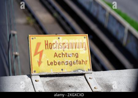 Gelbes Schild mit roter Aufschrift in deutscher Hochspannung Achtung Lebensgefahr auf einer Brücke über eine Eisenbahnstrecke Stockfoto