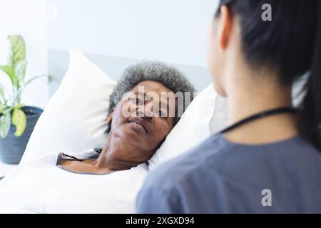Eine ältere afroamerikanische Frau liegt in einem Krankenhausbett mit Kopierraum. Eine Krankenschwester sorgt für Pflege und hebt die mitfühlende Natur der Gesundheitsversorgung hervor. Stockfoto