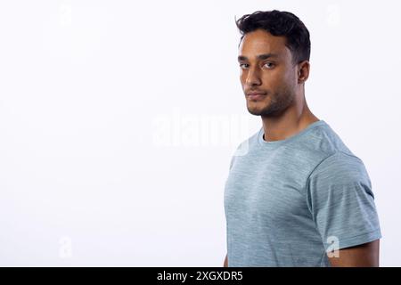 Junger birassischer Mann posiert selbstbewusst in einem Studio-Setting auf weißem Hintergrund, mit Kopierraum. Seine lässige Kleidung deutet auf eine entspannte und ansprechbare Kleidung hin Stockfoto