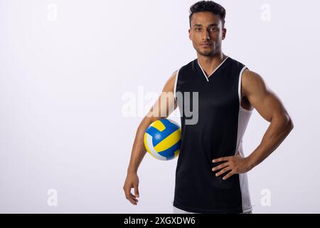 Junger birassischer Mann posiert selbstbewusst mit einem Volleyball auf weißem Hintergrund, mit Kopierraum. Er trägt Sportkleidung, was Sport oder f andeutet Stockfoto
