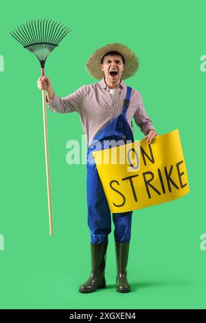 Protest gegen männlichen Landwirt, der ein Plakat mit STREIK- und Rechen-Text vor grünem Hintergrund hält Stockfoto