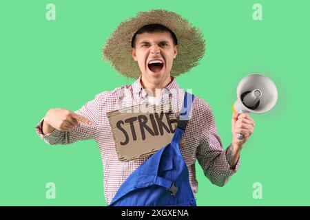 Protestierender männlicher Bauer mit Megaphon, der auf ein Plakat mit WORTSCHLAG auf grünem Hintergrund zeigt Stockfoto