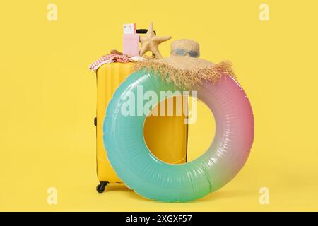 Verpackter Koffer, aufblasbarer Ring und Strandzubehör auf gelbem Hintergrund Stockfoto