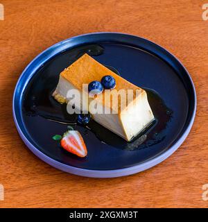 Creme Caramel Flan Dessert mit Heidelbeeren und Erdbeeren auf Karamellsauce wird auf einem eleganten Teller serviert Stockfoto