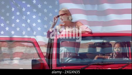 Bild der Flagge der usa über afroamerikanischen und kaukasischen Freundinnen, die im Auto sitzen Stockfoto