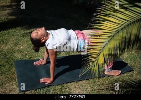 Frau übt Yoga im Freien, posiert auf einer Matte in einem sonnigen Garten. Entspannung, Fitness und Verbindung mit der Natur. Stockfoto