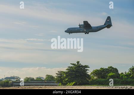 Balikpapan, Indonesien - 14. Juni 2024. Ein Lockheed C-130J Hercules Militärtransportflugzeug fliegt über einen wunderschönen Strand mit üppigem Grün Stockfoto