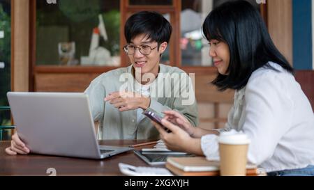 Ein kluger junger asiatischer Mann hat ein Treffen, um ein gemeinsames Projekt mit seinem Kollegen in einem Café zu besprechen, mit dem Finger auf einen Laptop-Bildschirm zu zeigen und zu erklären Stockfoto