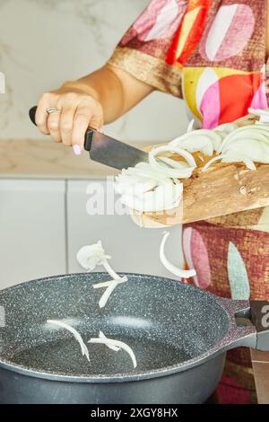 Eine Frau gibt gehackte Zwiebeln in eine Pfanne auf einem elektrischen Herd in ihrer Küche. Stockfoto