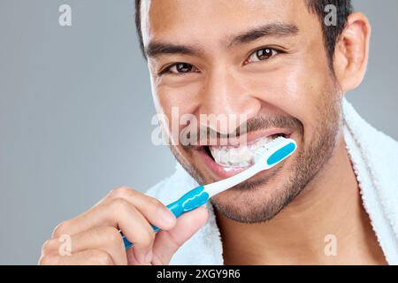 Zähneputzen, Pflege und Porträt des asiatischen Mannes im Studio auf grauem Hintergrund für Wellness. Zahnbürste, Zahnpasta und Lächeln mit Happy Stockfoto