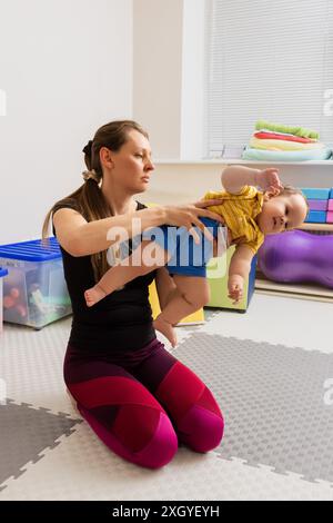 Physiotherapeut bei der Durchführung von Armzugübungen mit Säuglingen während neurologischer pädiatrischer Untersuchung. Therapeut, der mit einem Baby in einer Rehabilitation arbeitet Stockfoto