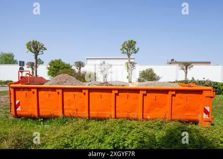 Container, orangefarbener Sprung für Bauschutt, der auf einer Wiese steht, Deutschland Stockfoto