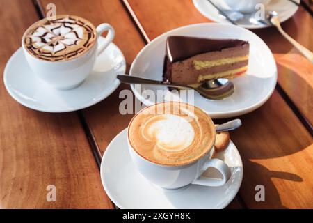 Zwei Tassen heißer Cappuccino-Kaffee und Schokoladenmousse-Kuchen auf Holztisch im Café. Frisches belebendes Getränk und süßes Dessert. Stockfoto
